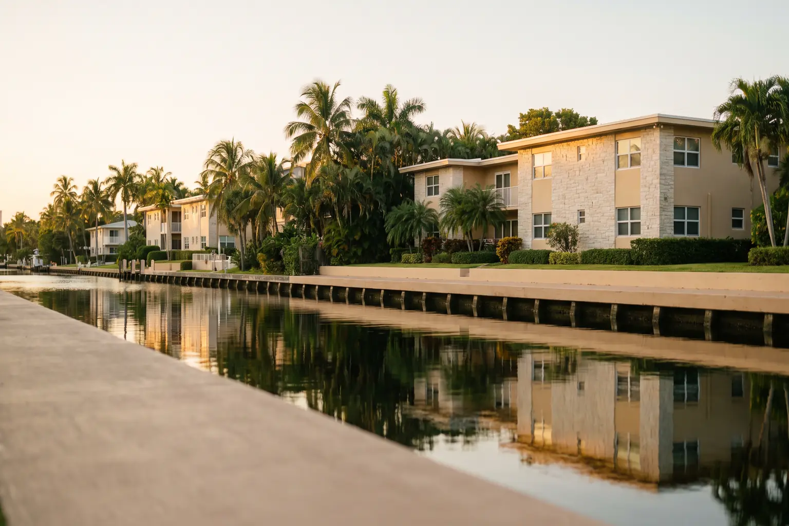 A Fort Lauderdale residential canal at golden hour with waterfront apartments set back behind palms
